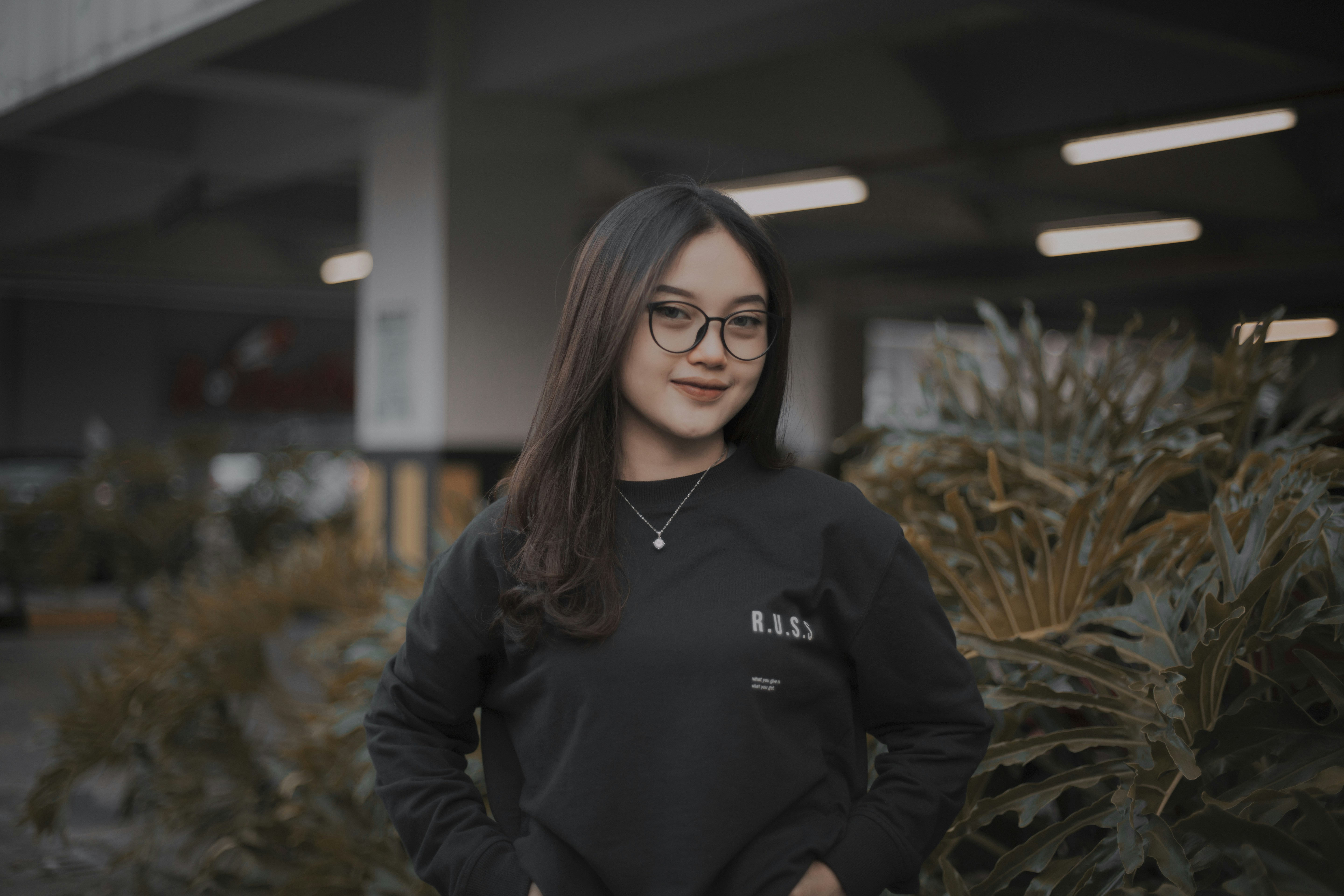 a woman wearing glasses standing in front of plants
