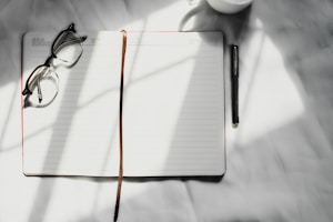 a notebook with a pen, glasses and a cup of coffee