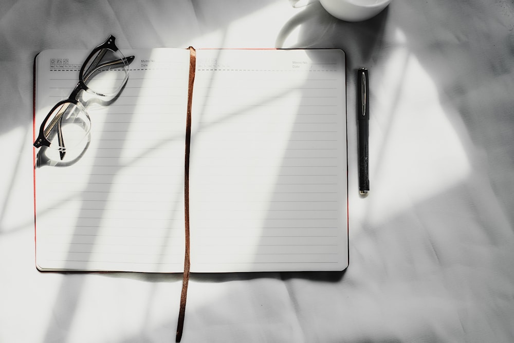 a notebook with a pen, glasses and a cup of coffee