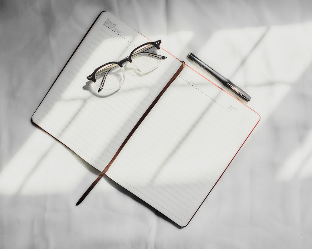 um caderno com uma caneta e óculos em cima dele