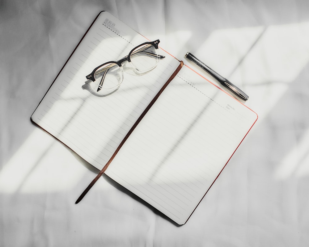 a notebook with a pen and glasses on top of it