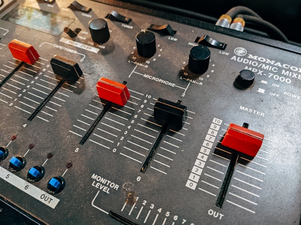 A close-up view of an audio mixer, featuring several sliders and knobs used for adjusting sound levels. The sliders are marked with numeric levels, including sections labeled 'Microphone' and 'Master'. The mixer is labeled 'Monacor Audio/Mic Mixer MPX-7000'.