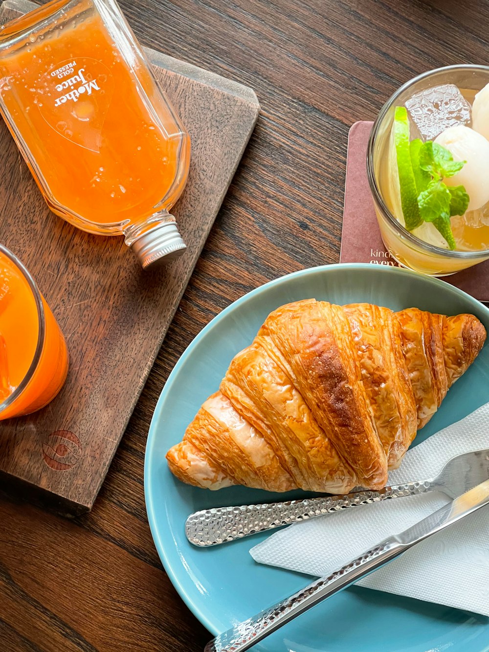 a croissant on a blue plate next to a glass of orange juice
