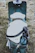 A vintage-style scooter with a brown leather double seat is parked on grassy ground. A white helmet with the inscription 'HIGHWAY 1' is placed on the seat, secured by a chain and padlock to the frame of the scooter. The scooter has a retro design with a teal body and chrome accents.