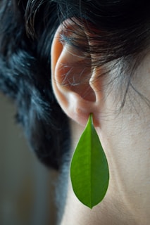a close up of a person's ear with a green leaf hanging from it