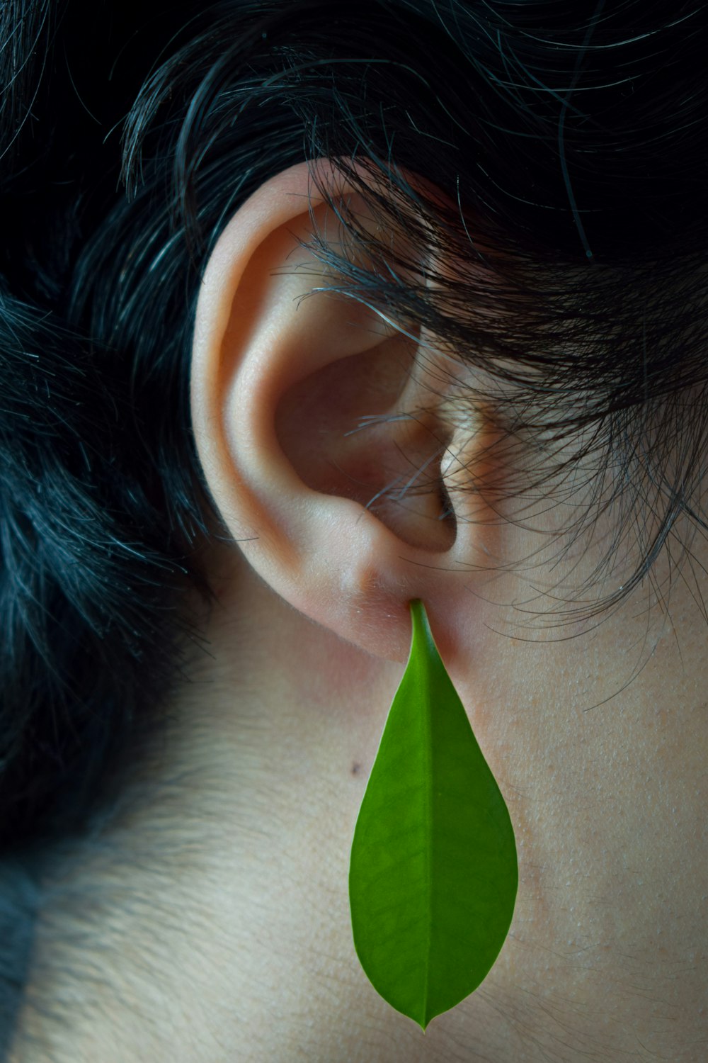 a close up of a person's ear with a green leaf hanging from it