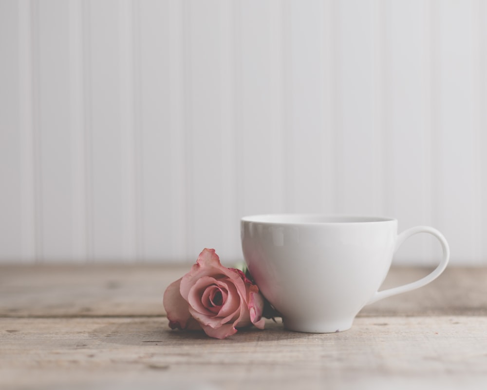 um copo branco com uma rosa rosa em uma mesa de madeira