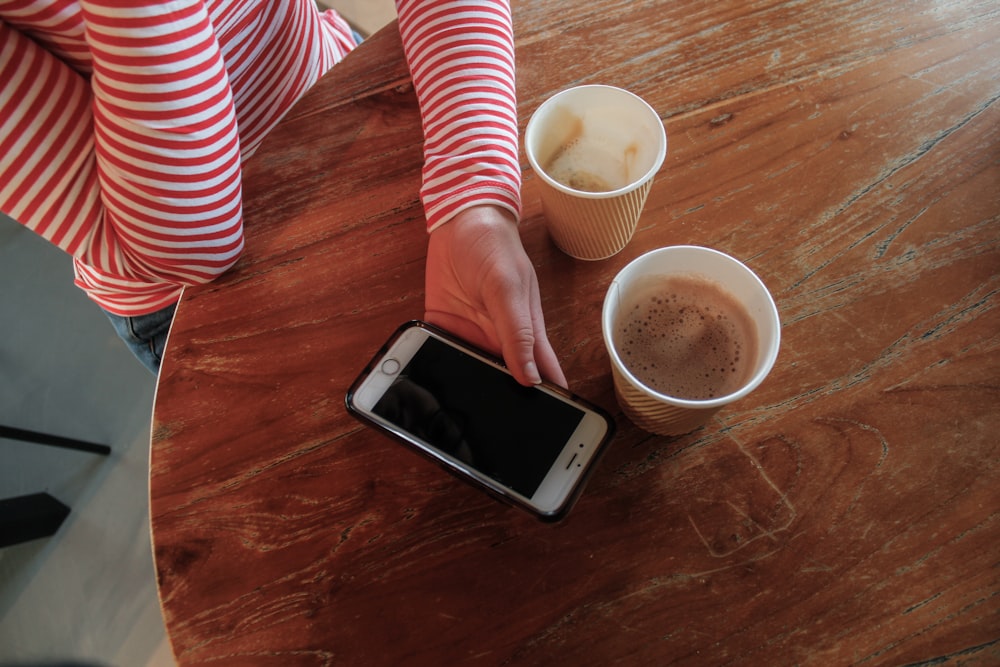 a woman holding a cell phone next to two cups of coffee