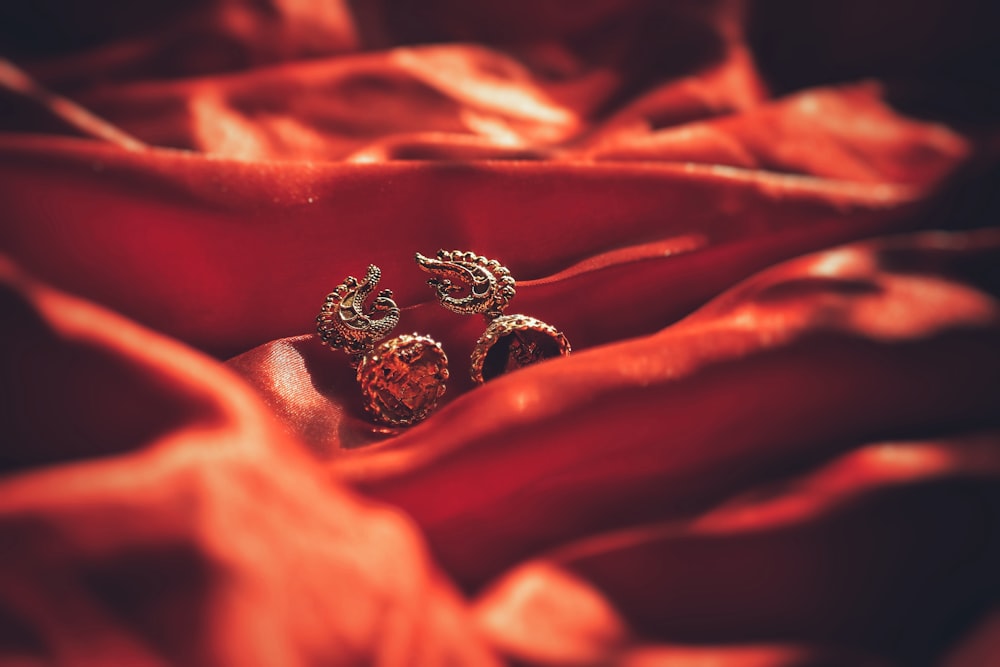 a close up of a pair of earrings on a red cloth