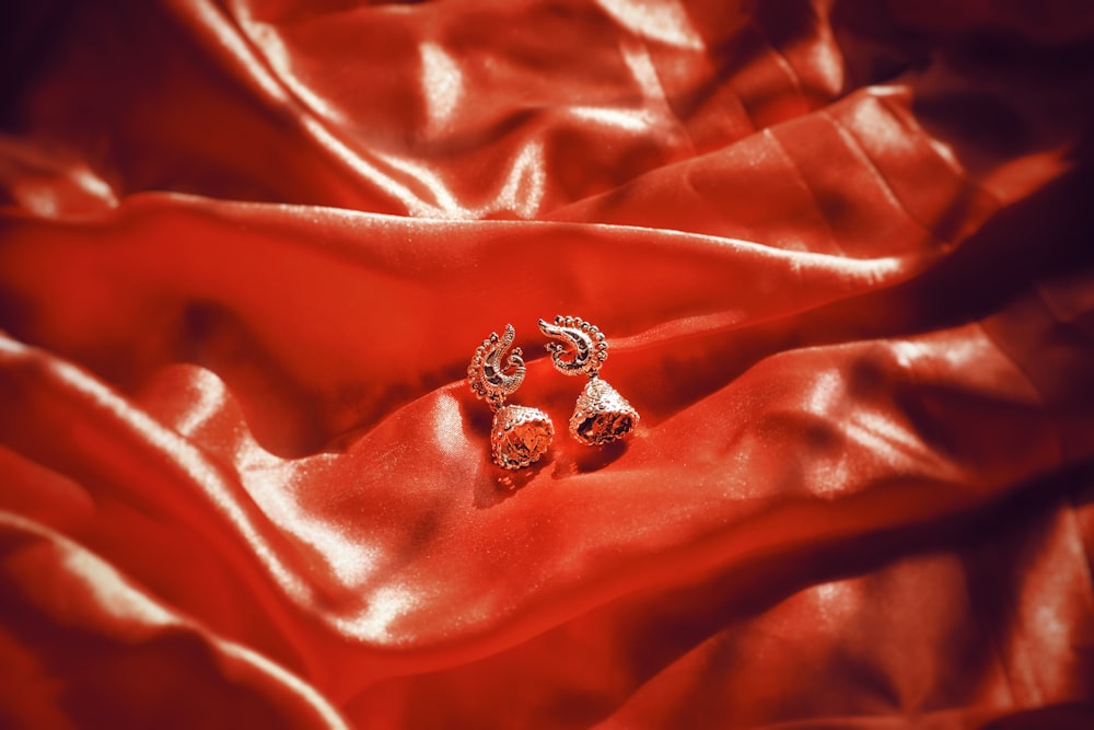 a pair of earrings sitting on top of a red cloth