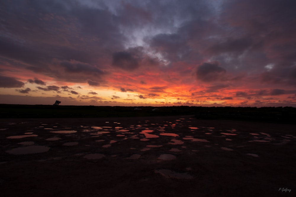 the sun is setting over a field with puddles of water