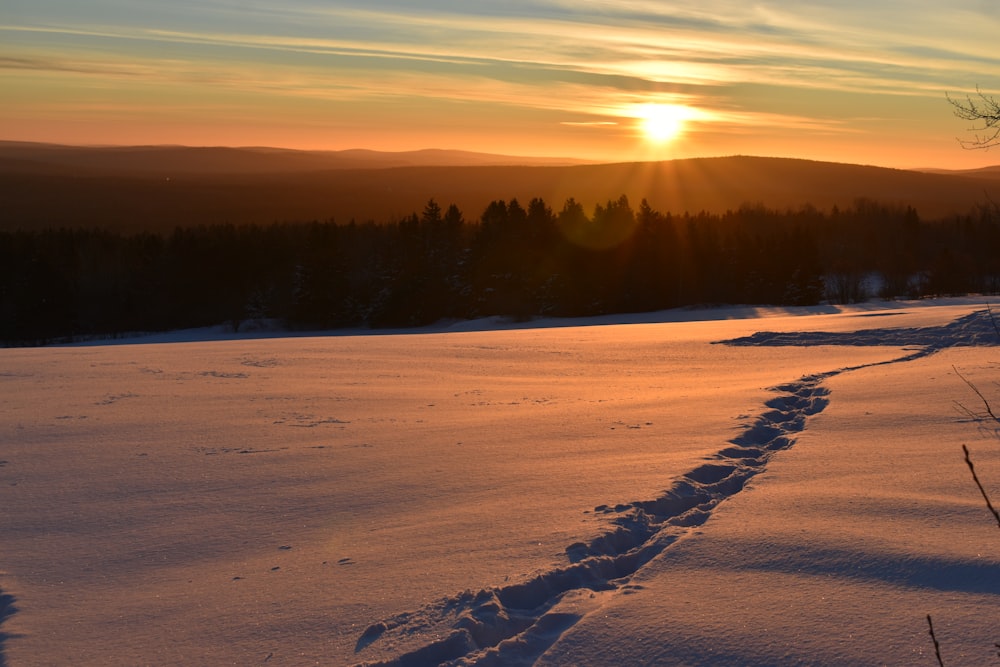 the sun is setting over a snowy field