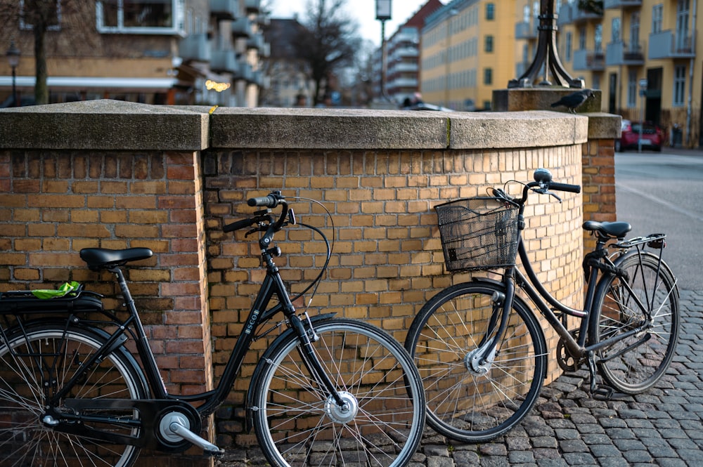 duas bicicletas estacionadas ao lado de uma parede de tijolos