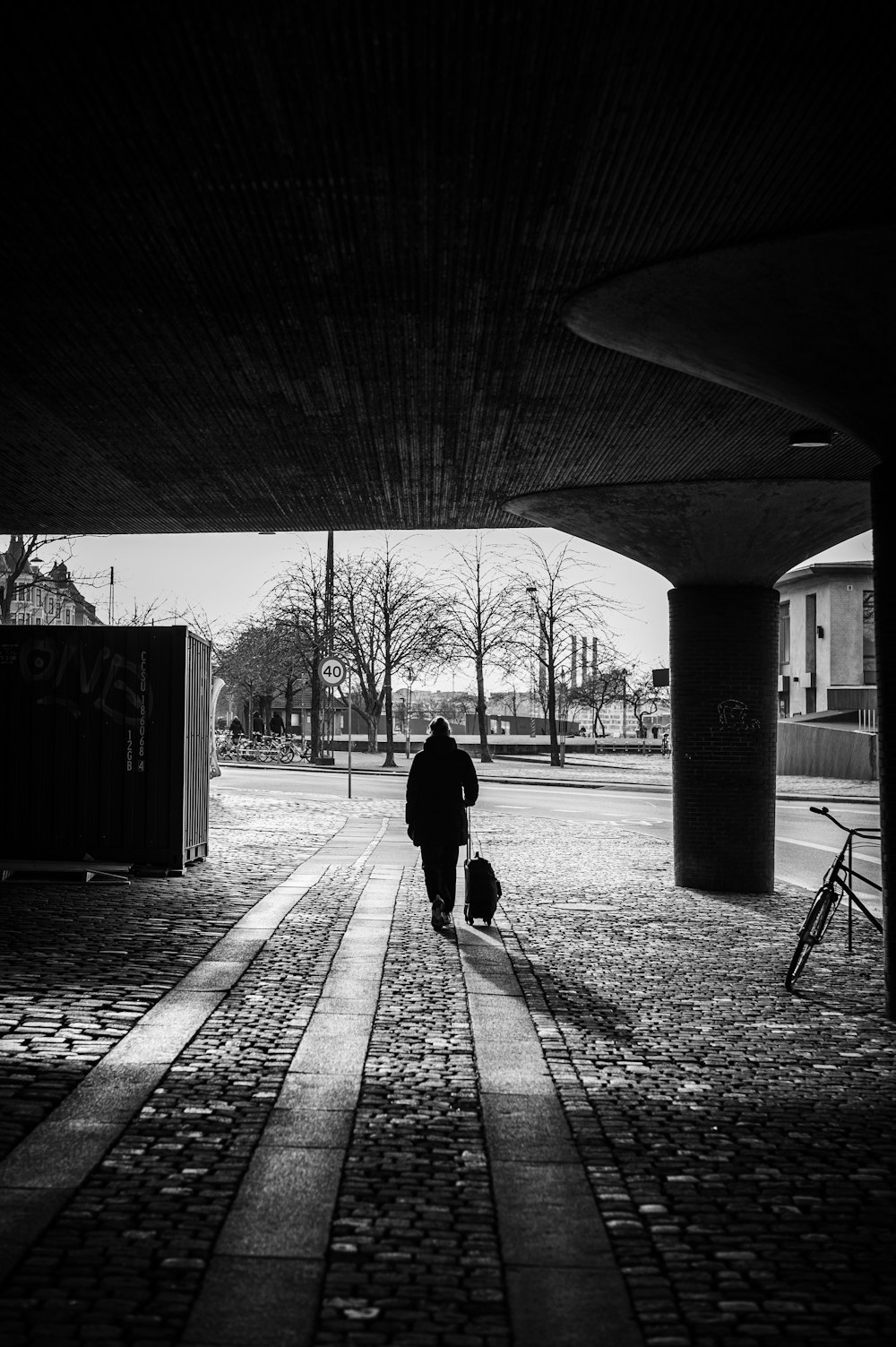 Eine Person mit einem Koffer geht unter einer Brücke