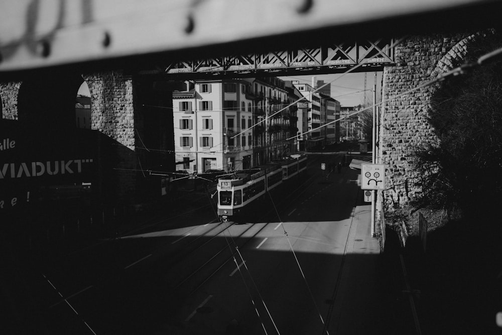 a black and white photo of a train going under a bridge