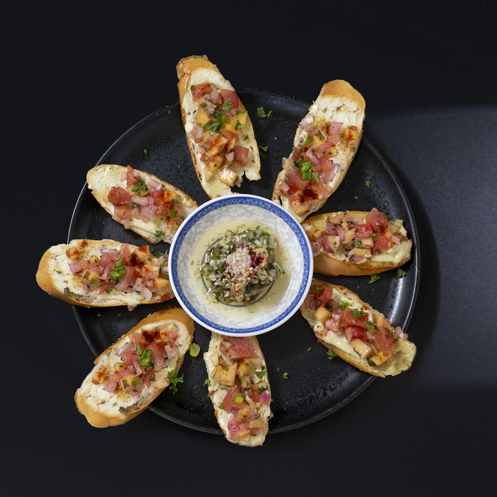 a black plate topped with slices of bread covered in toppings