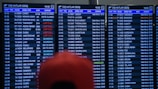 Three airport departure boards displaying various international flight details such as times, destinations, gate numbers, and status updates. The information is shown in white text on a dark background, with special indications like 'Last Call' and 'Boarding' highlighted in red. The text is in both English and another language. A blurry red object is partially visible in front of the boards.