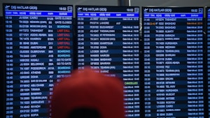 Three airport departure boards displaying various international flight details such as times, destinations, gate numbers, and status updates. The information is shown in white text on a dark background, with special indications like 'Last Call' and 'Boarding' highlighted in red. The text is in both English and another language. A blurry red object is partially visible in front of the boards.