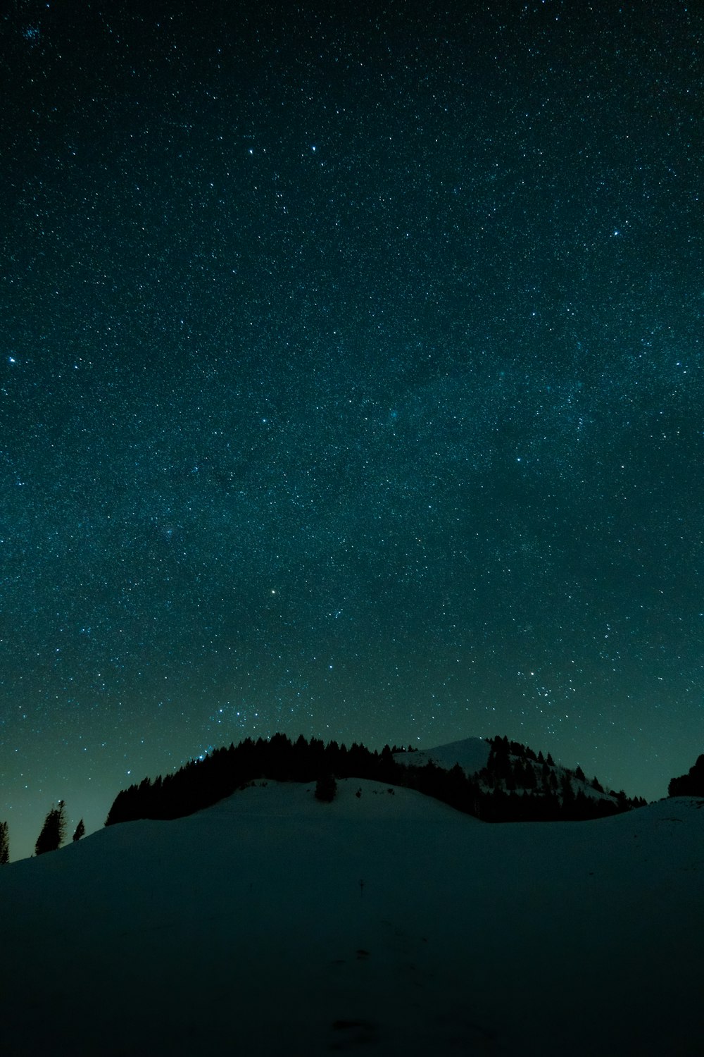 the night sky with stars above a snowy hill