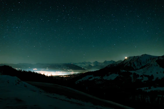 A tranquil Bhutanese valley under a vast, star-filled midnight blue sky with soft golden light on distant peaks.