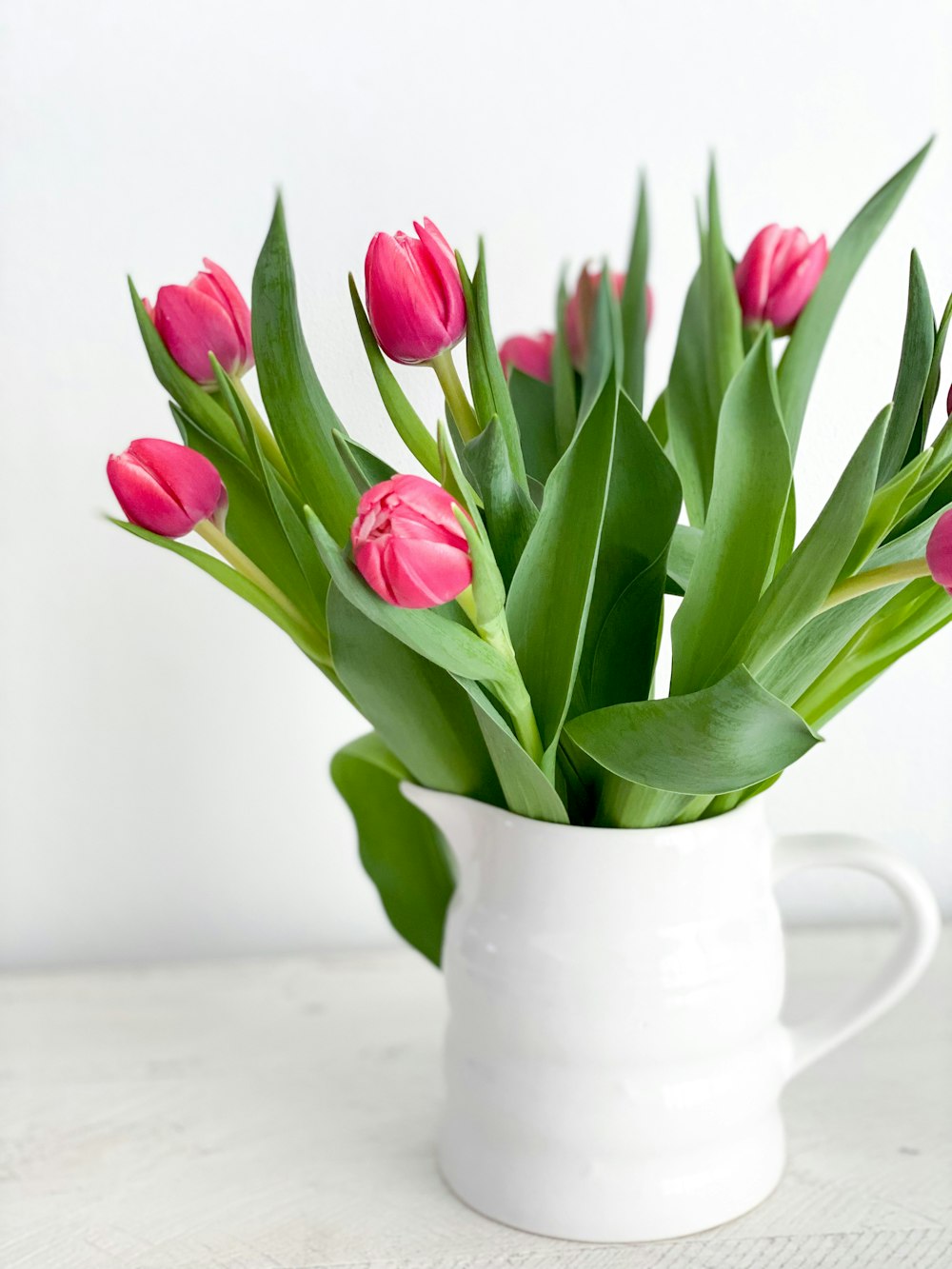 a white vase filled with pink flowers on top of a table