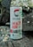 A can of Celsius Peach Vibe energy drink is placed outdoors on a rustic wooden surface, surrounded by small stones. The can features bold red and green graphics with text highlighting its benefits like essential energy, sugar-free content, and metabolism acceleration.