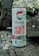 A can of Celsius Peach Vibe energy drink is placed outdoors on a rustic wooden surface, surrounded by small stones. The can features bold red and green graphics with text highlighting its benefits like essential energy, sugar-free content, and metabolism acceleration.