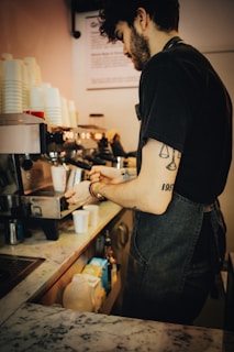 Barista with tattoos preparing coffee on professional espresso machine.