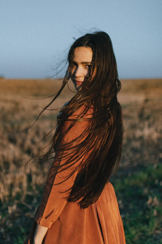 a woman with long hair standing in a field