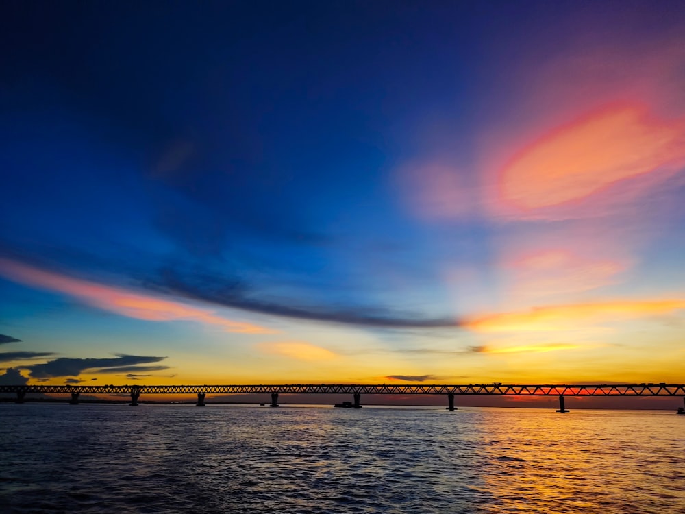 the sun sets over a bridge over a body of water