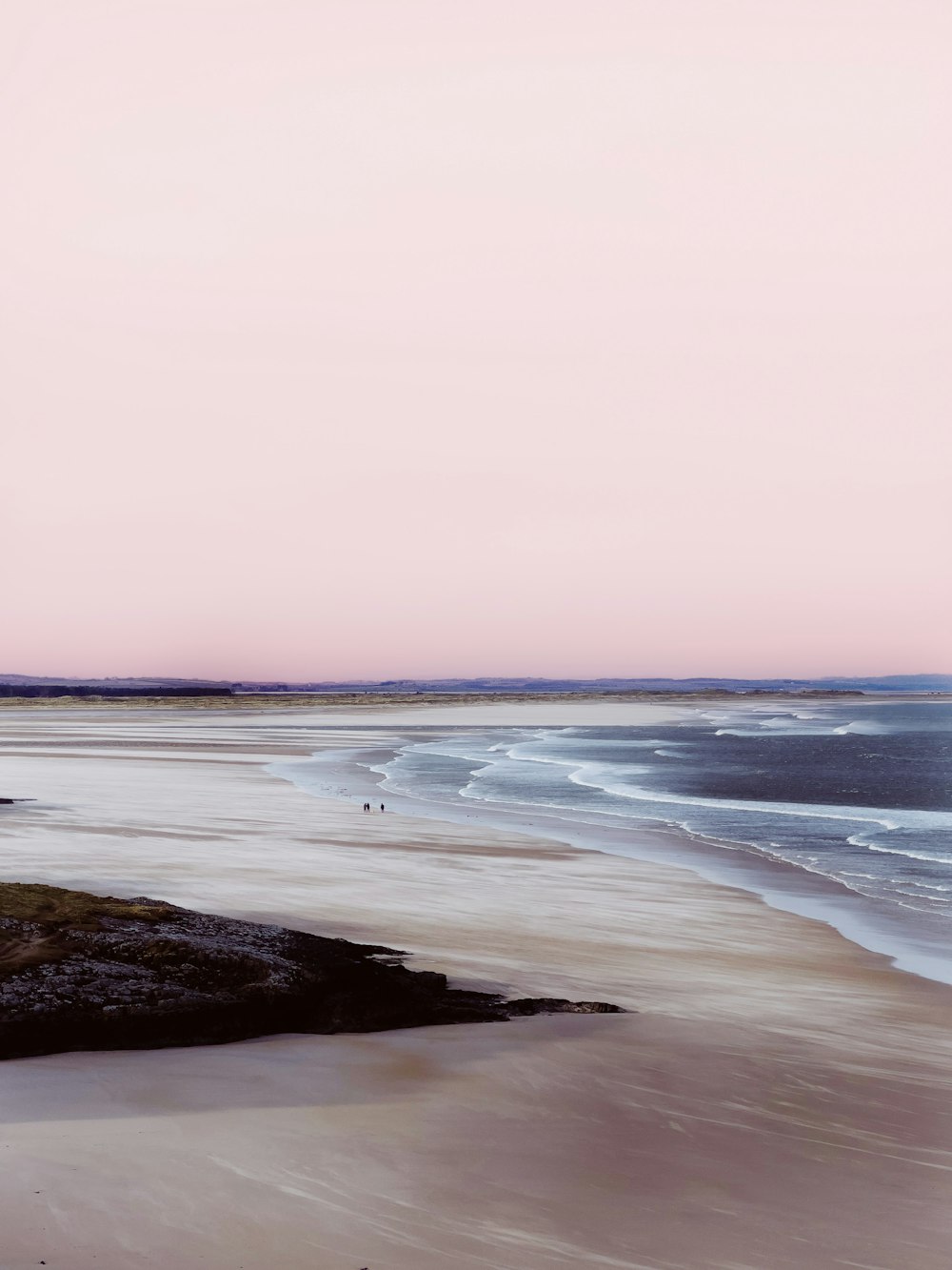 a pink sky over a sandy beach with waves