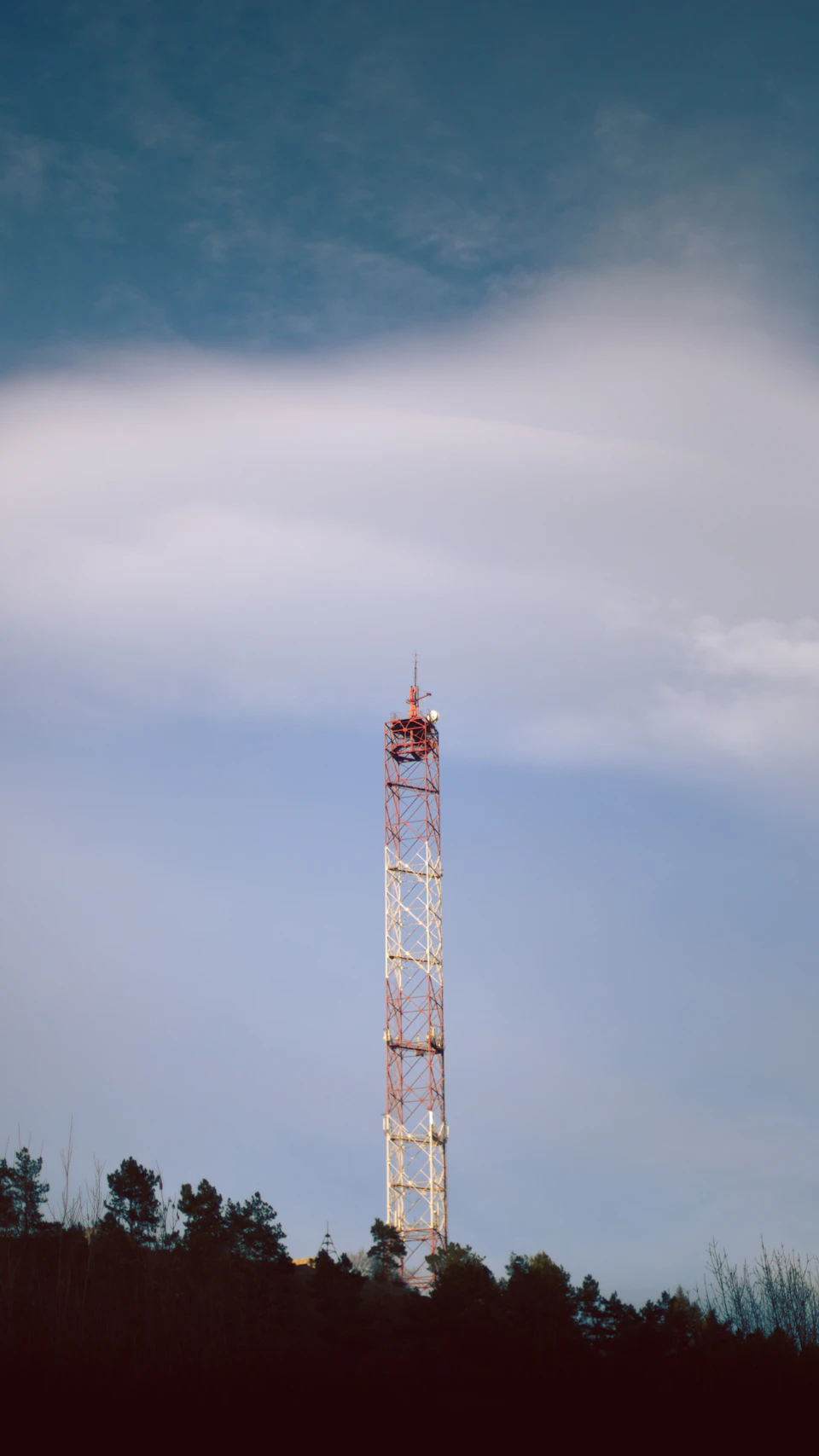 Tall white and red radio tower stands against clear blue sky with wispy clouds