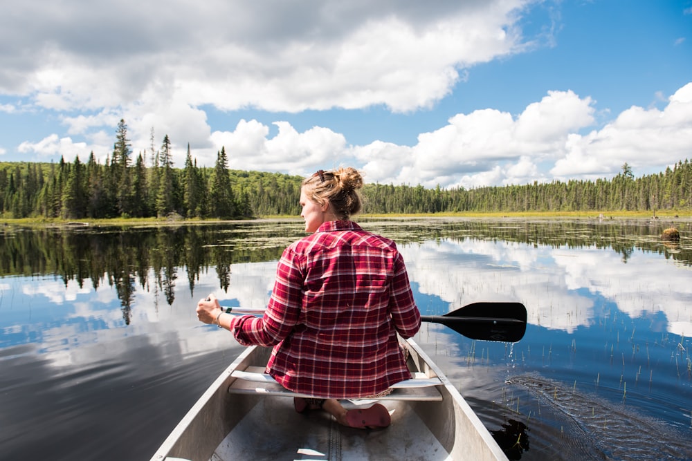a woman in a plaid shirt paddling a canoe