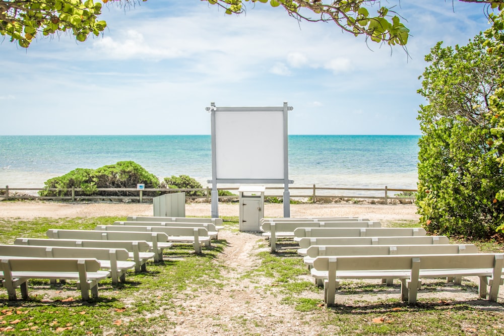 a row of white benches sitting next to a beach