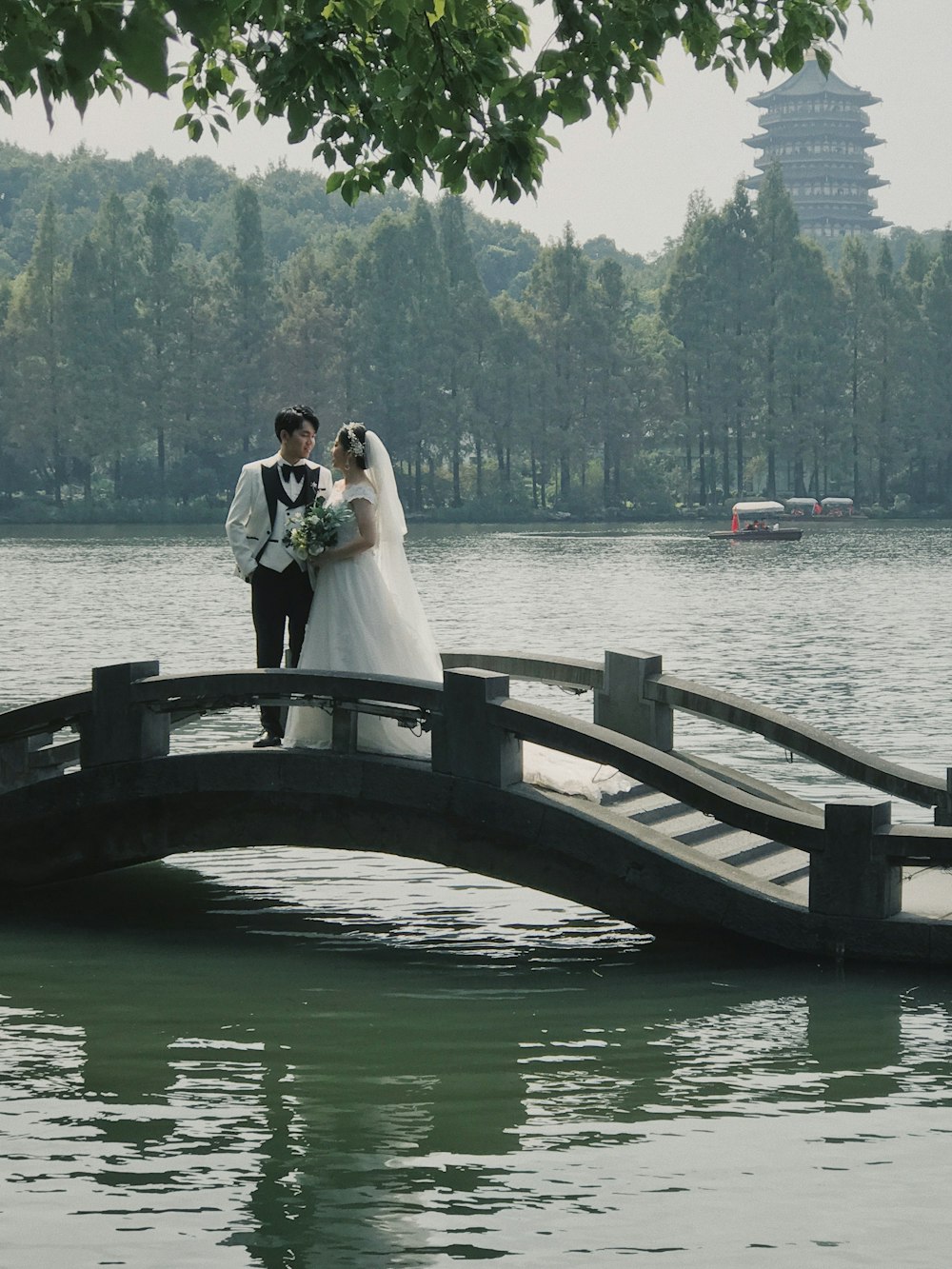 a bride and groom standing on a bridge over a lake