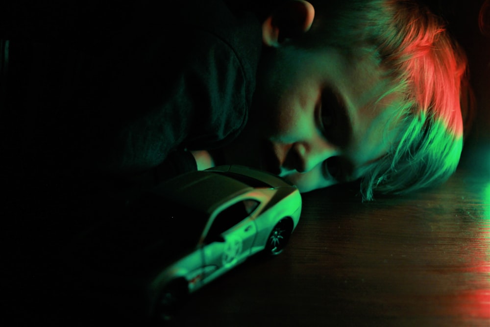 a young boy laying on the floor next to a toy car