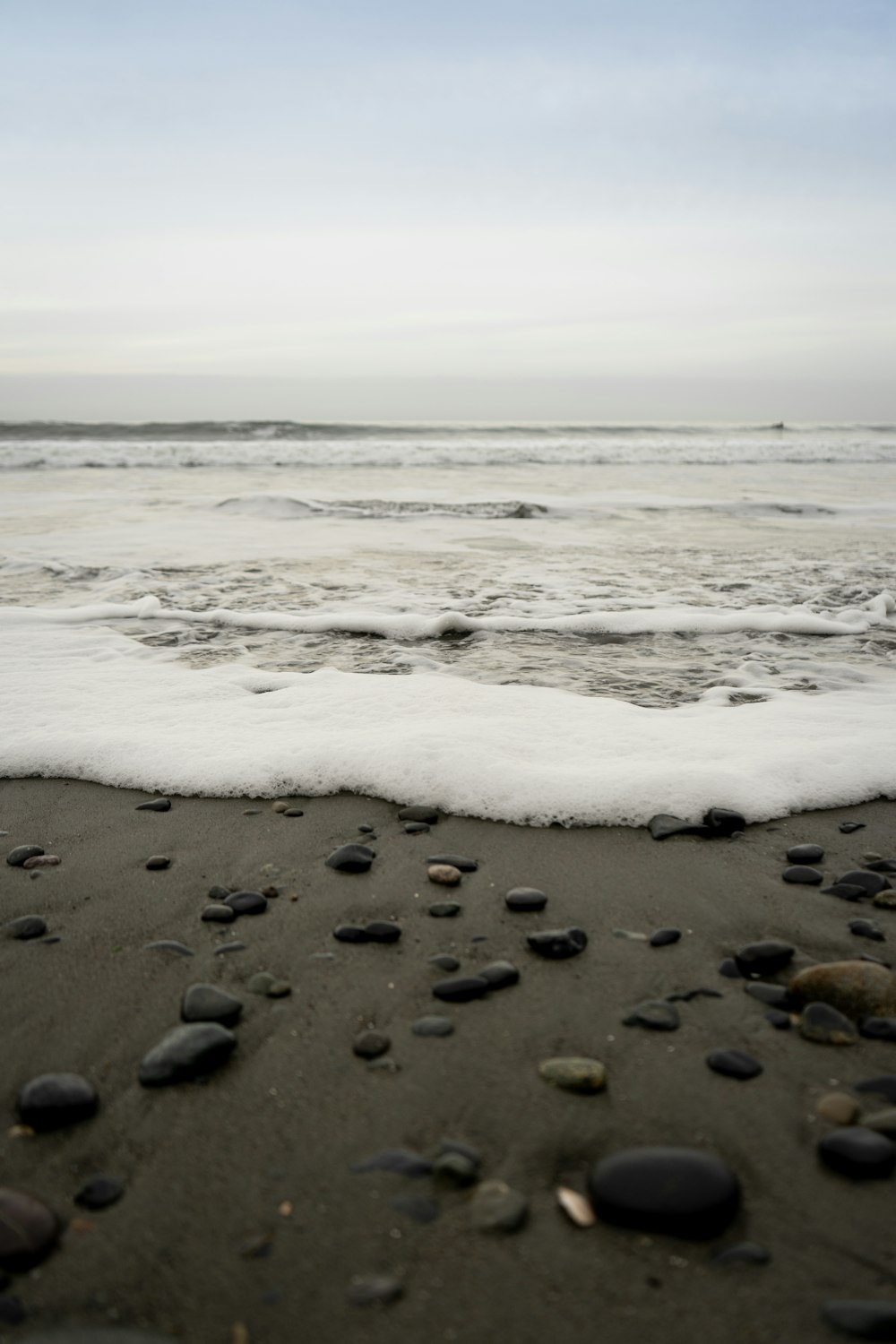 a beach with a wave coming in and some rocks in the sand