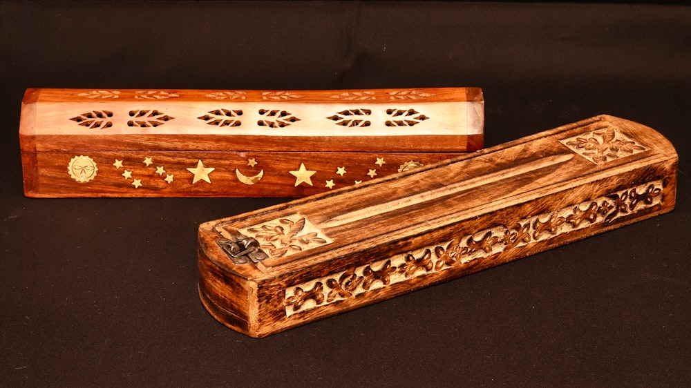 two wooden boxes with designs on them on a black surface