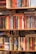 A variety of books is arranged on several wooden shelves, featuring multiple colors and genres. The books are stacked both vertically and horizontally, with some titles clearly visible, including classic and contemporary works.