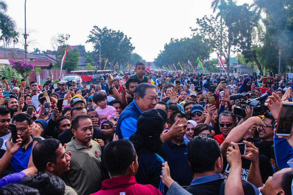 a crowd of people standing around a man on a cell phone