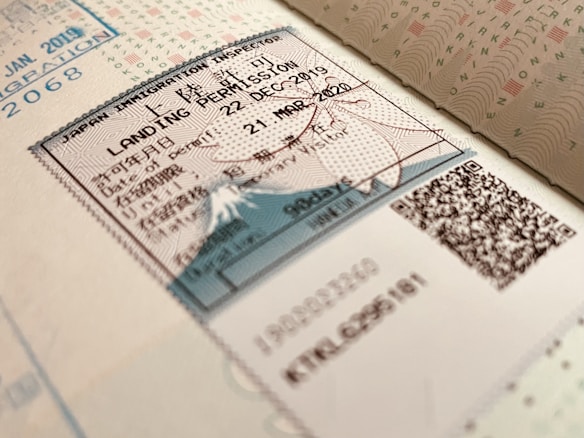 A close-up view of a Japanese immigration inspector's landing permission stamp on a passport page, featuring a document with text in both Japanese and English. The stamp includes the date of entry and validity, with visible QR codes and security features embedded in the design.