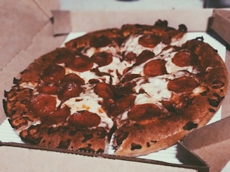 A freshly baked pepperoni pizza with melted cheese and crispy edges is placed inside an open cardboard pizza box.