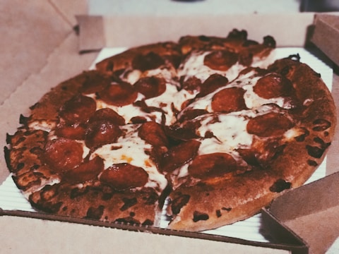 A freshly baked pepperoni pizza with melted cheese and crispy edges is placed inside an open cardboard pizza box.