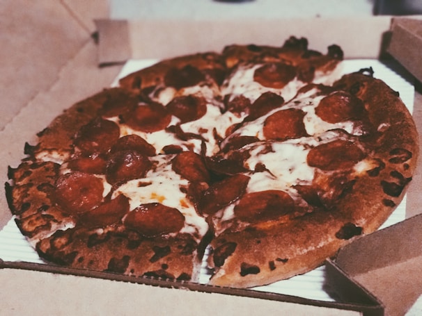 A freshly baked pepperoni pizza with melted cheese and crispy edges is placed inside an open cardboard pizza box.