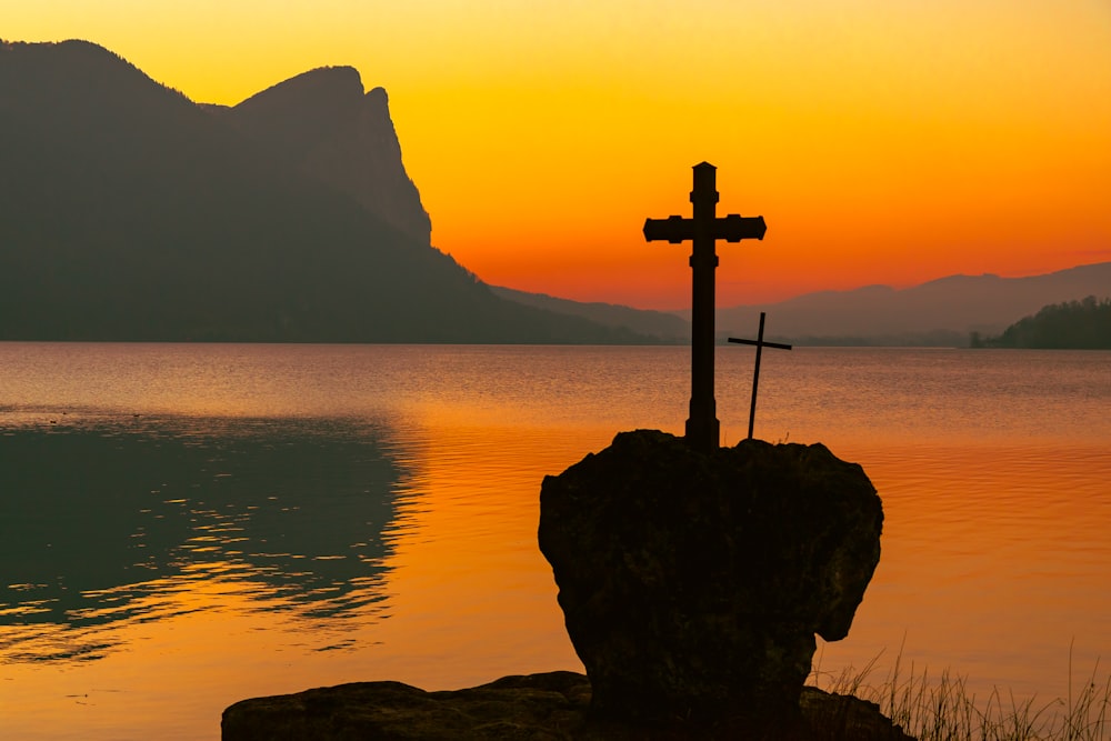 a cross sitting on top of a rock next to a body of water