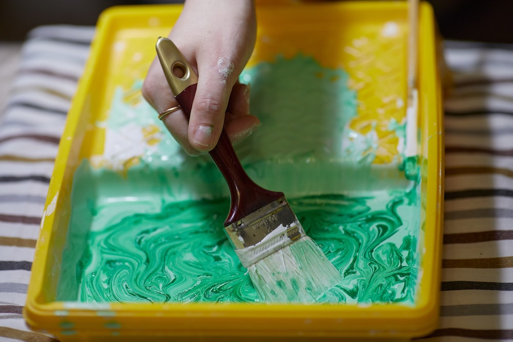 a person holding a paint brush in a yellow tray