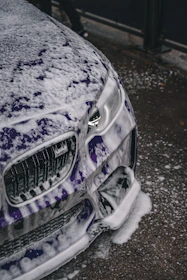 Close-up of a shiny car being hand-washed with soap suds on the body.