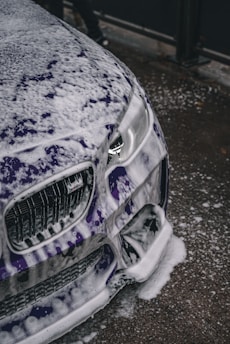 Close-up of a car being carefully hand-washed with foam and microfiber cloth.