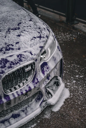 Close-up of a glossy car hood being carefully washed with rich, foamy car shampoo.