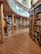 A spacious library with wooden floors and shelves, filled with a diverse collection of books. The architecture includes curved shelves and grand columns, providing an elegant and scholarly atmosphere. A glass railing separates sections of the library, and there is a computer or device stand placed near the shelves.